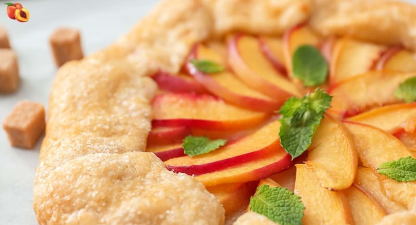 Freshly baked peach crostata featuring a flaky, golden crust, arranged with sliced peaches and topped with fresh mint leaves