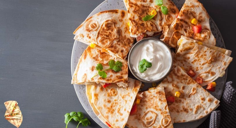 Classic quesadilla slices filled with cheese and vegetables, served on a plate with sour cream in the center, with cilantro