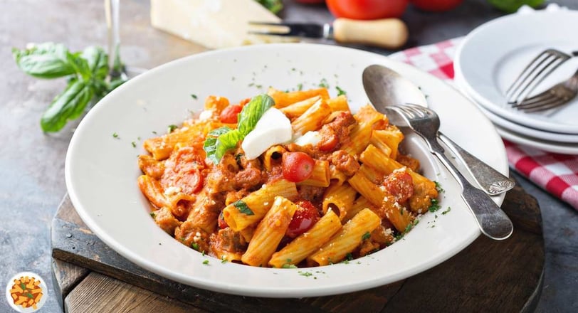 Rigatoni with creamy Bolognese sauce, cherry tomatoes, basil, and ricotta in a white bowl