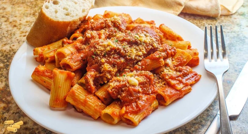 Rigatoni pasta smothered in a savory Bolognese sauce, garnished with Parmesan cheese, served with a slice of bread