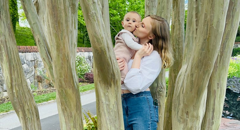 A mother holding her baby in a tree, kissing her on the cheek while the baby looks at the camera, showing loving mother-child