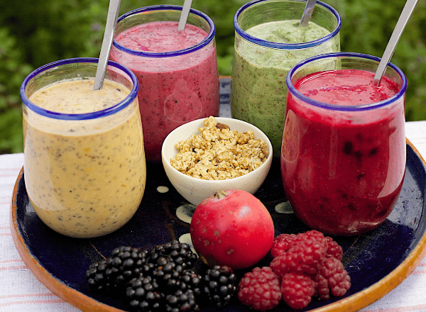 four smoothie glasses in tray with some fruits