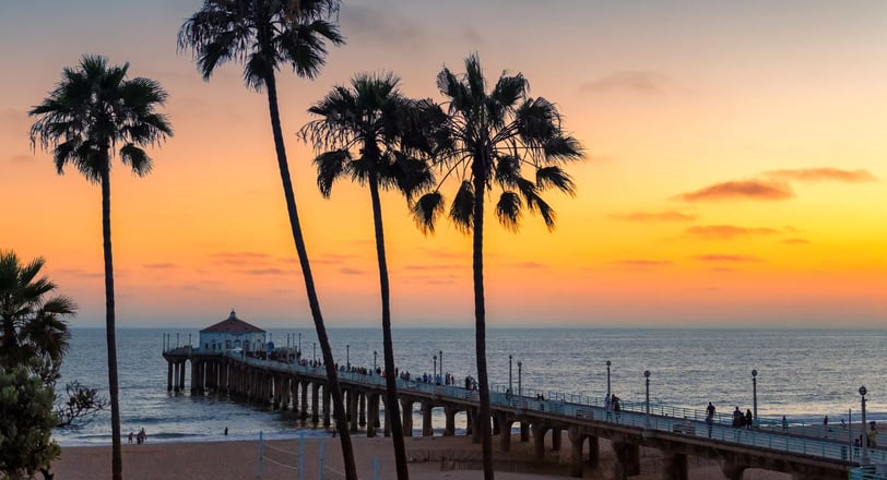 Pier de Santa Monica ao entardecer, com palmeiras ao fundo e o céu colorido pelo pôr do sol na Califórnia