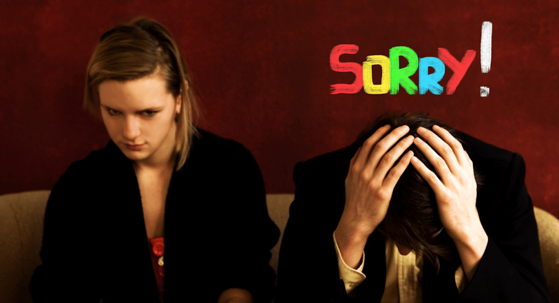A womand and a man sitting on a couch with a sign that says sorry