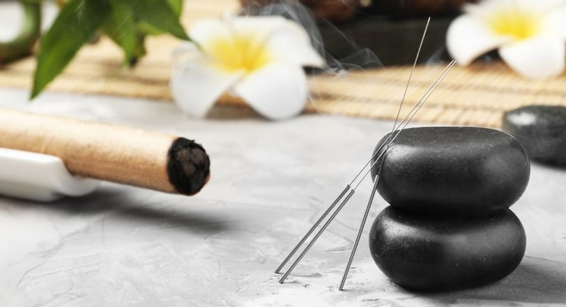 Acupuncture needles tilted on a table and Ayurvedic stones