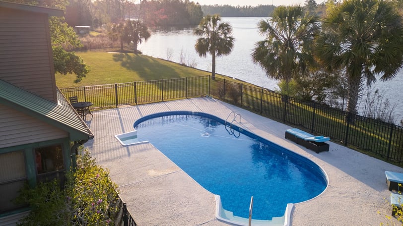 a pool with a fenced in area with a bench and chairs