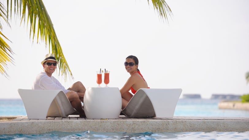 two people sitting on lounge chairs in front of a pool