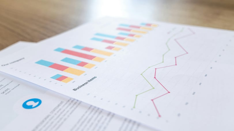 Two overlapping sheets of paper on a tabletop, the top one covered in graphs, a bar graph and a line graph.