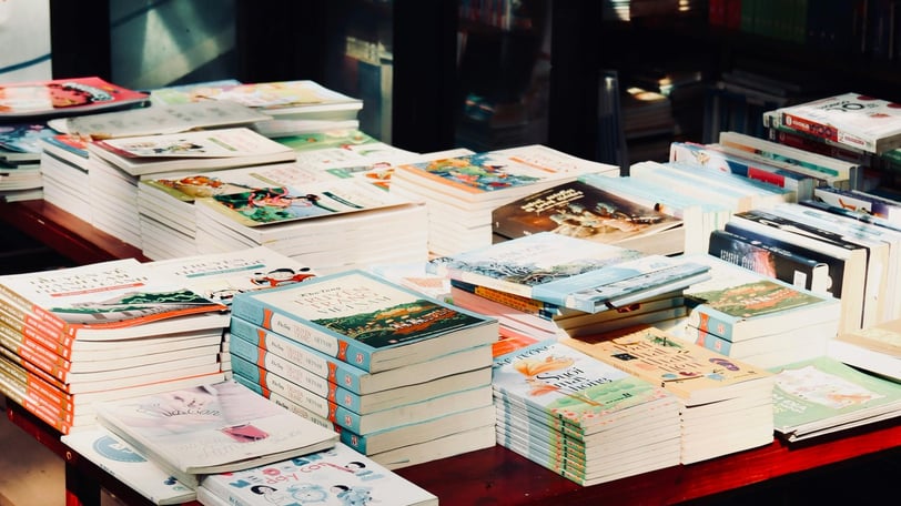 A selection of piles of books upon a table in what appears to be a bookshop.