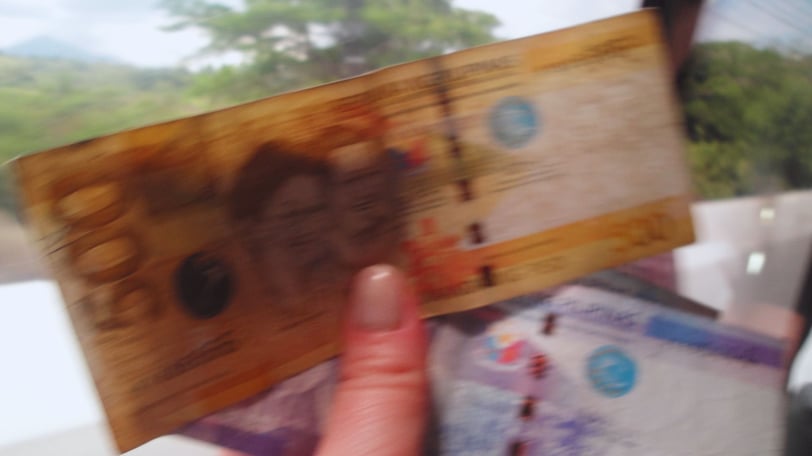 Autora segurando notas de peso filipino, com cenário local ao fundo.