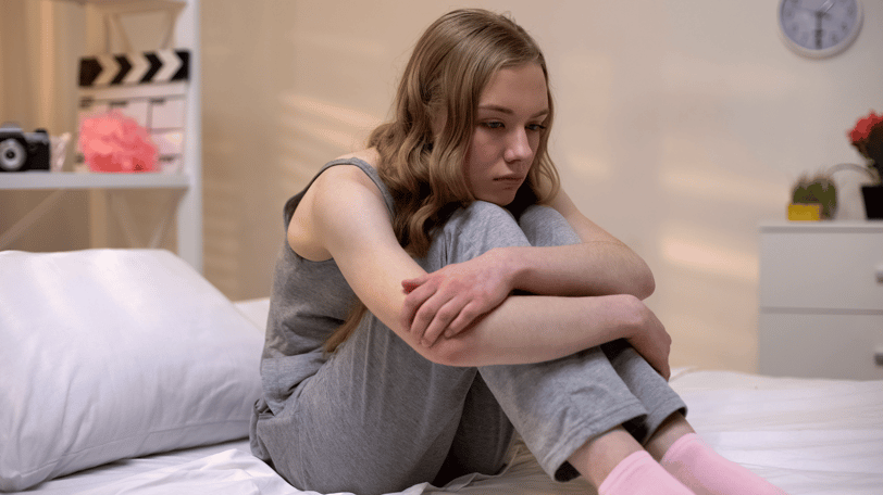 Mujer jovencita sentada en su cama pensando acerca de los sentimientos de ansiedad que experimenta