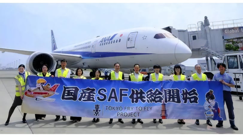ANA機の前で反射ベスト姿の関係者らが「国産SAF供給開始」と記された横断幕を掲げている。2025年7月、堺市の製油所で量産された国産SAFが羽田空港定期便に本格供給されたニュース報道用写真。