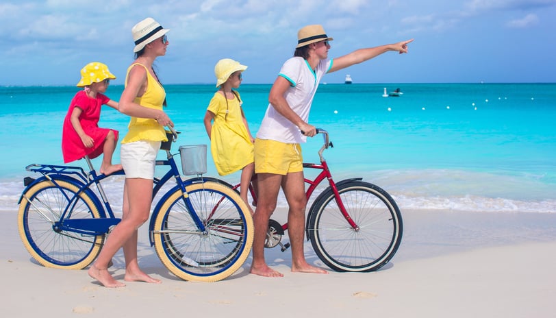Family travelers riding bicycles on a tropical beach