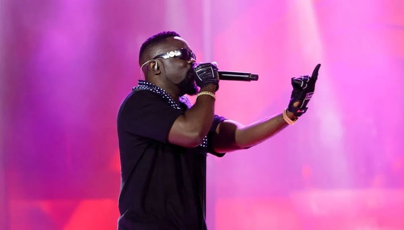 Sarkodie performing on stage in a black top and black shades.