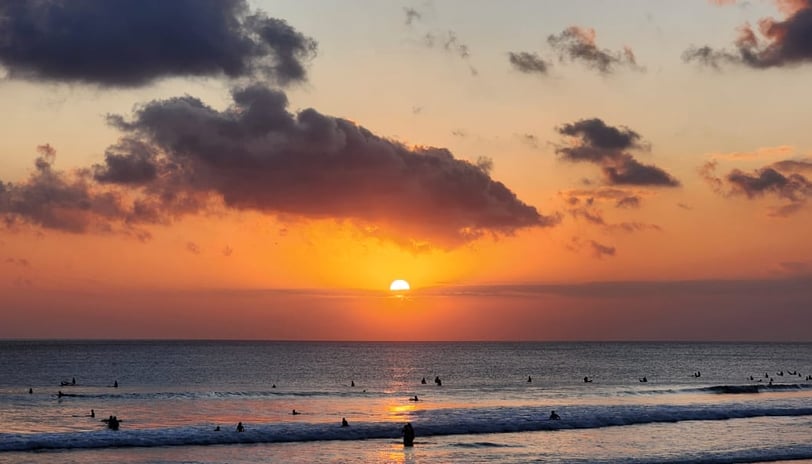 a sunset over kuta beach with people surfing