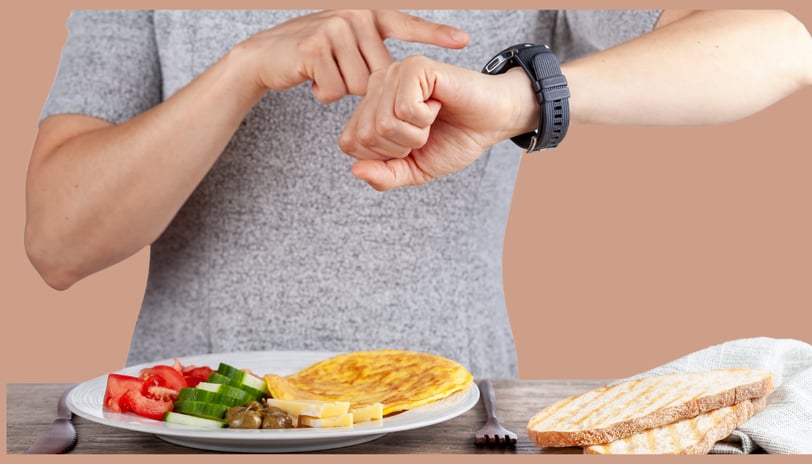 Pessoa olhando para o relógio enquanto se prepara para uma refeição com legumes e pão, representando o jejum intermitente.