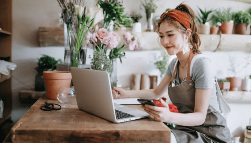 A small businesswoman ownwer sitting on her desk with her laptop and a mobile phone on her hand