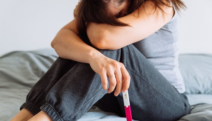 a woman sitting on a bed with a pregnancy test in her hand