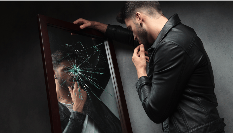 a man in a leather jacket is looking at a broken mirror