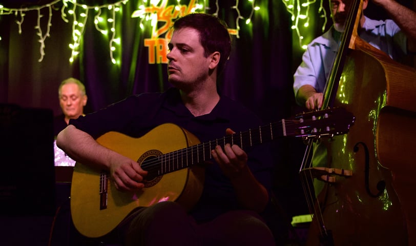 a man (rob coleman) playing acoustic guitar with a drummer and bassist