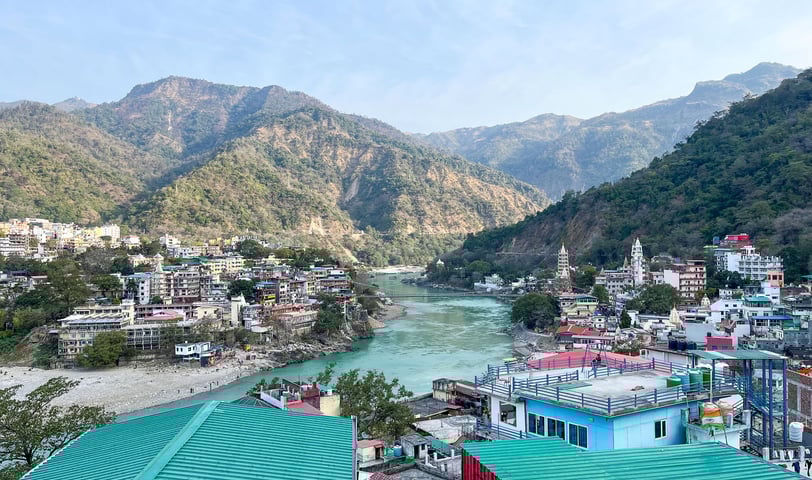 Scenic rooftop view overlooking the mountains and the cityscape of Rishikesh, India, under a clear sky.