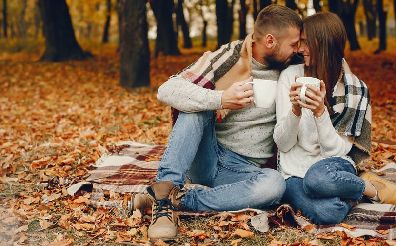 a man and woman sitting on a blanket in the woods