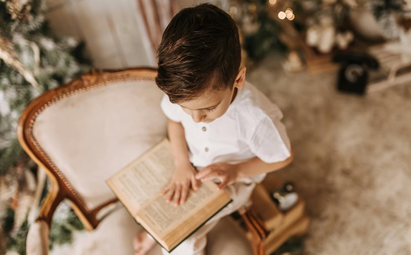 a young boy is sitting in a chair and reading a book