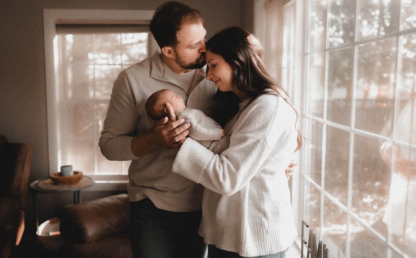 Mom and dad standing by their window with their newborn