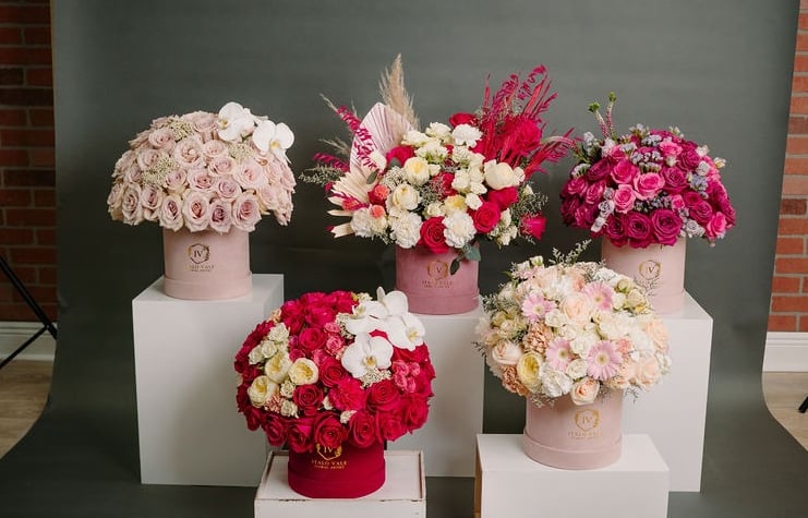 Variety of elegant floral arrangements featuring pink roses, red roses, white orchids, and mixed flowers in decorative boxes