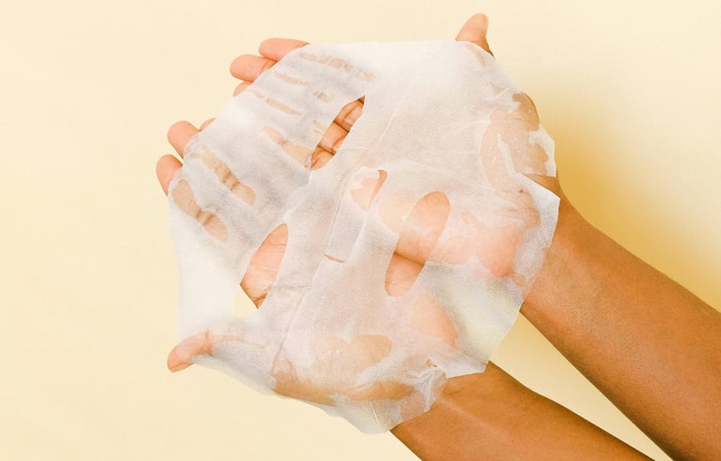 someone holding a beauty face mask with both hands against a yellow wall.