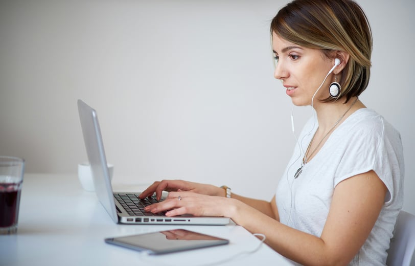 a woman with headphones, in a white shirt is sitting at a desk, typing