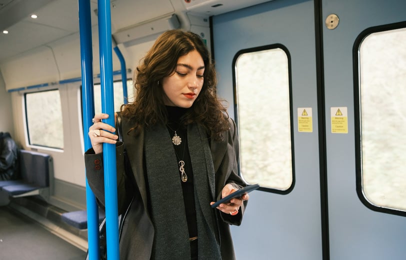 A woman standing on a train looking at her cell phone.