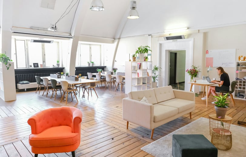 A modern co-working space with worktables, a red chair, and beige sofe