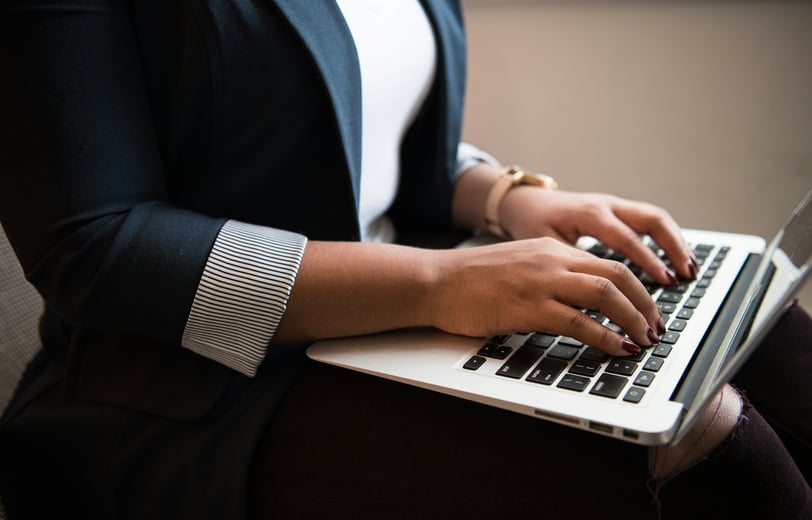 a woman in a white shirt and navy blazer sitting and using a laptop