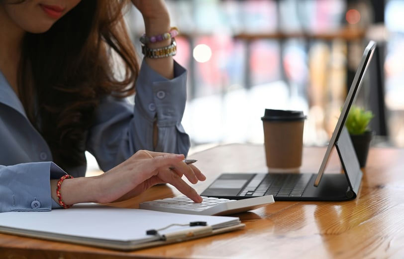 A woman sitting at a desk, holding a pen,  and working on a calculator