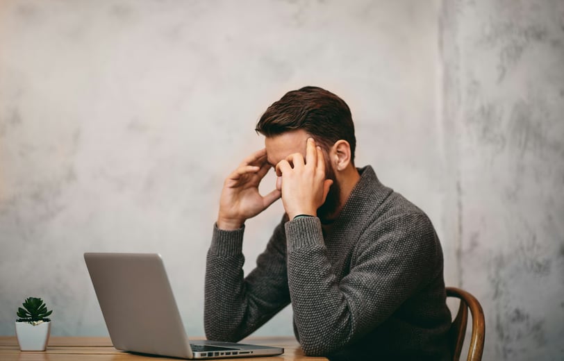 Stressed man sitting in front of a laptop and holding his head in his hands