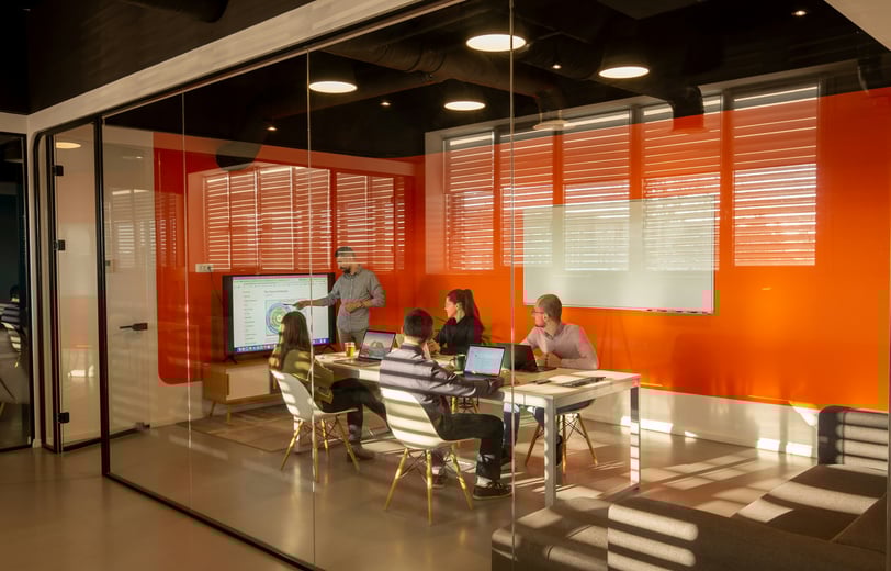 Wide shot through glass walls of a presentation during a ptojrvt team meeting of five people