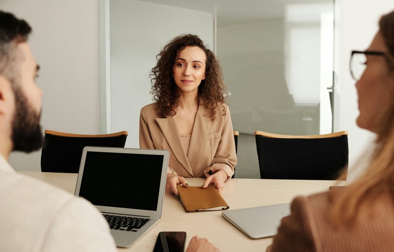 a woman in a business suit sitting at a table with a laptop and a man