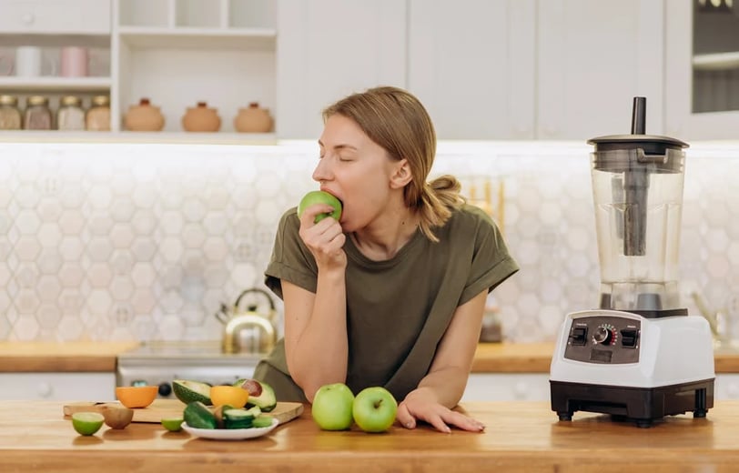 a woman is eating a green apple in a blender