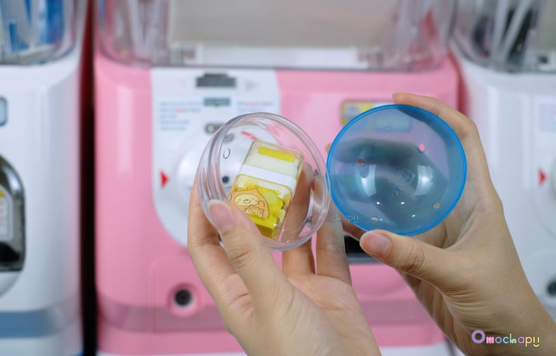 seseorang membuka kapsul gacha dari mesin gashapon