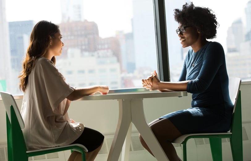 two women sitting at a table with a view of a city