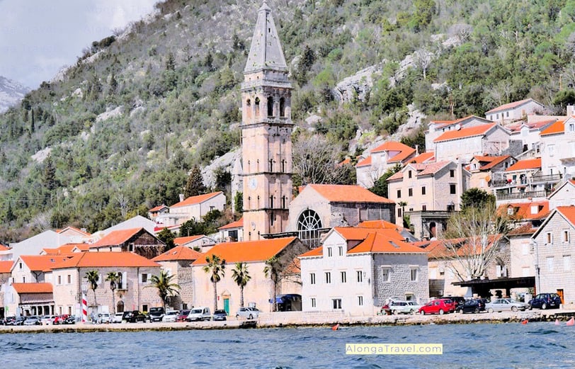 Tall pointed tower hoovering over medieval roofs of Perast, a short distance from Kotor.