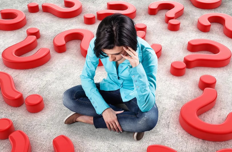 A thinking woman sitting on a floor with multiple red question marks around