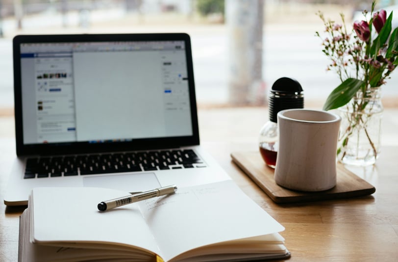 a laptop computer and a notebook with a pen and a cup of coffee