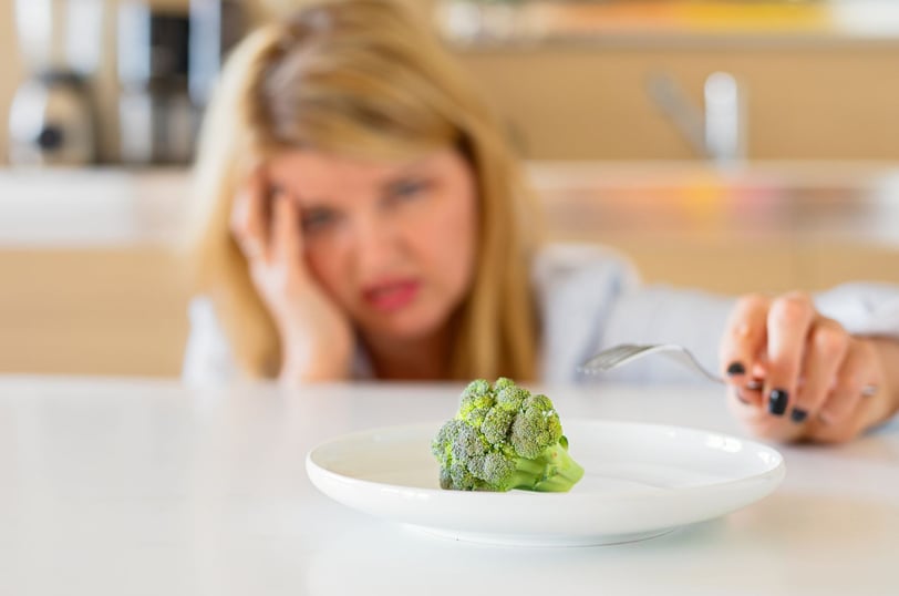 a woman sitting at a table with a plate of broccoli