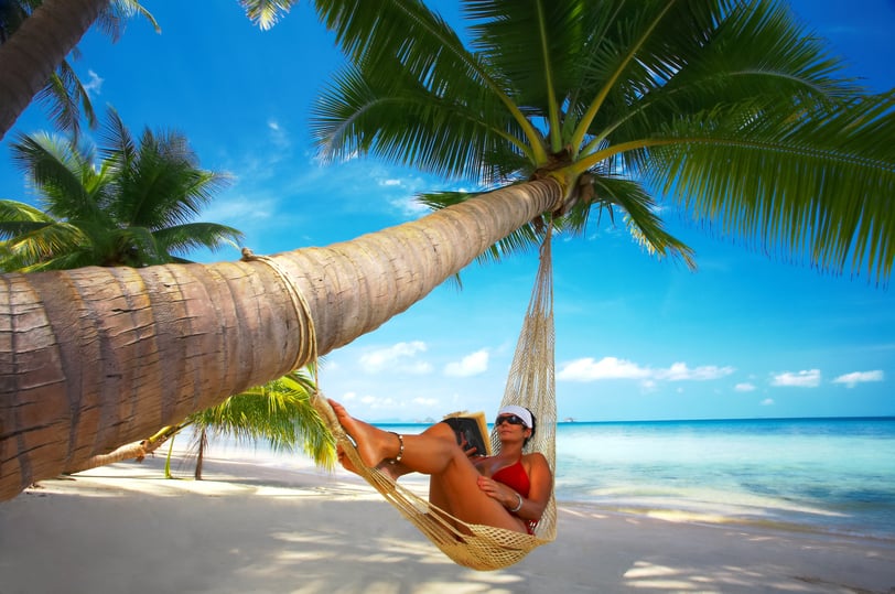 a woman in a bikini top sitting in a hammock reading a book