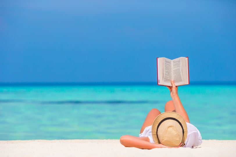 a woman reading a book while laying on the beach