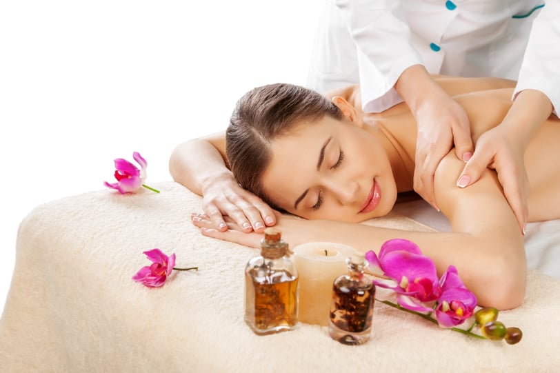 Mujer recibiendo masaje con aromaterapia en un entorno relajante, con aceites esenciales y flores, terapia natural para reduc