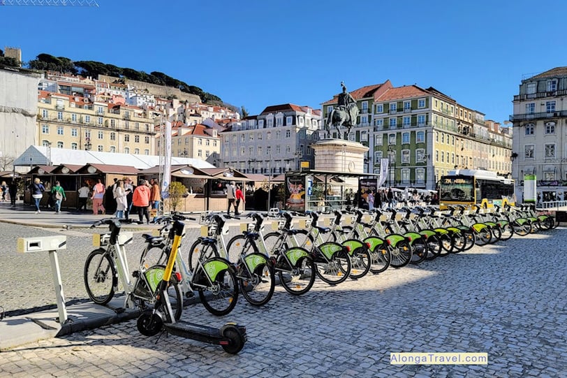 a row of green bikes and bus stops on a busy well planned square in Lisbon