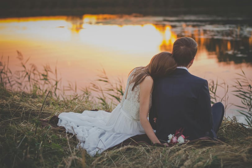 a bride and groom sitting on a grassy field